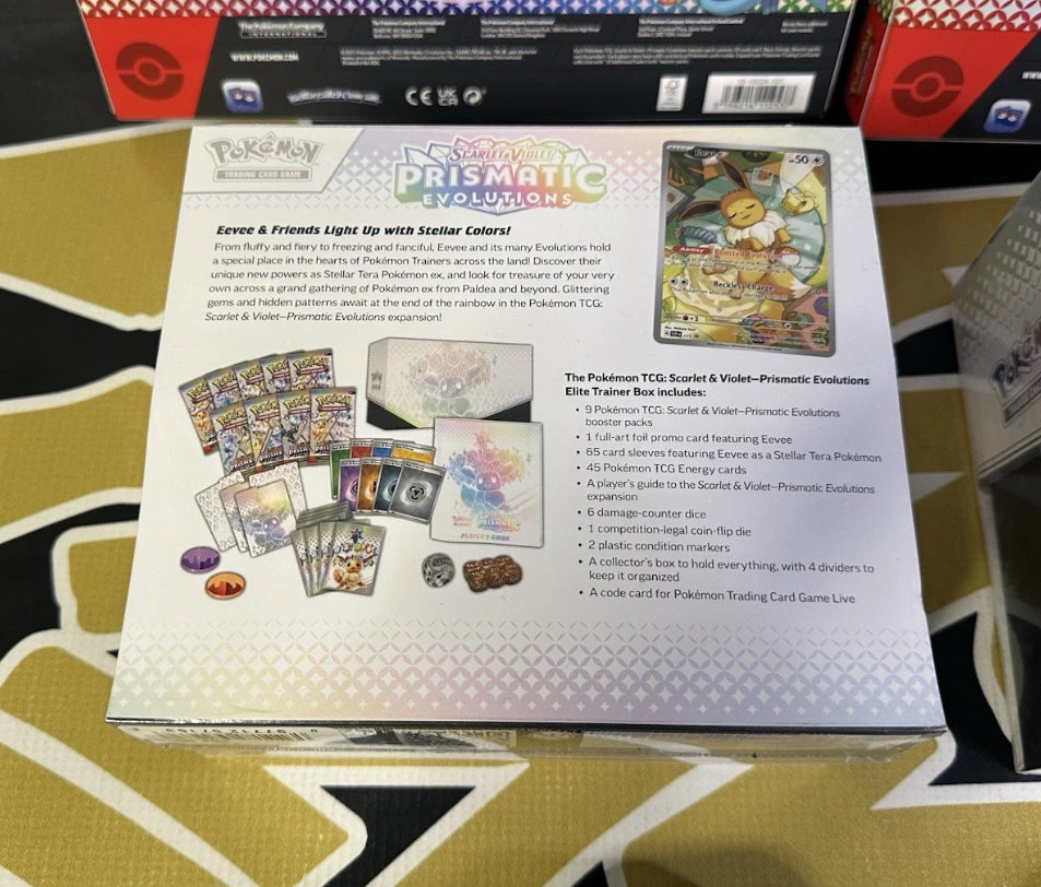 The Pokémon Scarlet & Violet Prismatic Evolutions Elite Trainer Box by Pokemon showcases a crystal-like Eevee surrounded by colorful gemstones, with a choking hazard warning displayed at the bottom.