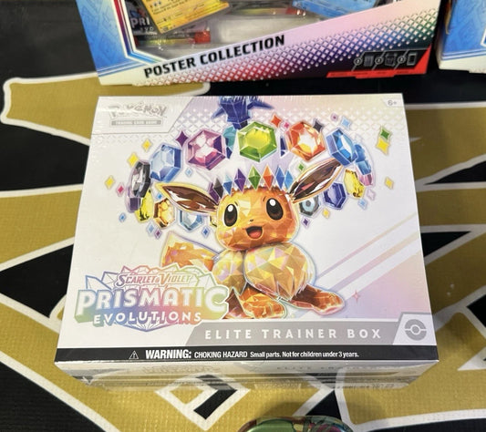 The Pokémon Scarlet & Violet Prismatic Evolutions Elite Trainer Box by Pokemon showcases a crystal-like Eevee surrounded by colorful gemstones, with a choking hazard warning displayed at the bottom.